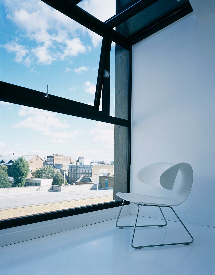 Weisser Schalenstuhl im Designerstil auf weißem Boden vor Fensterfront mit Ausblick