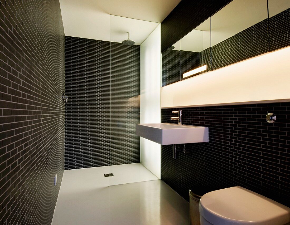 Dramatic bath with black tiled walls and recessed strip lighting in the wall over the wash basin