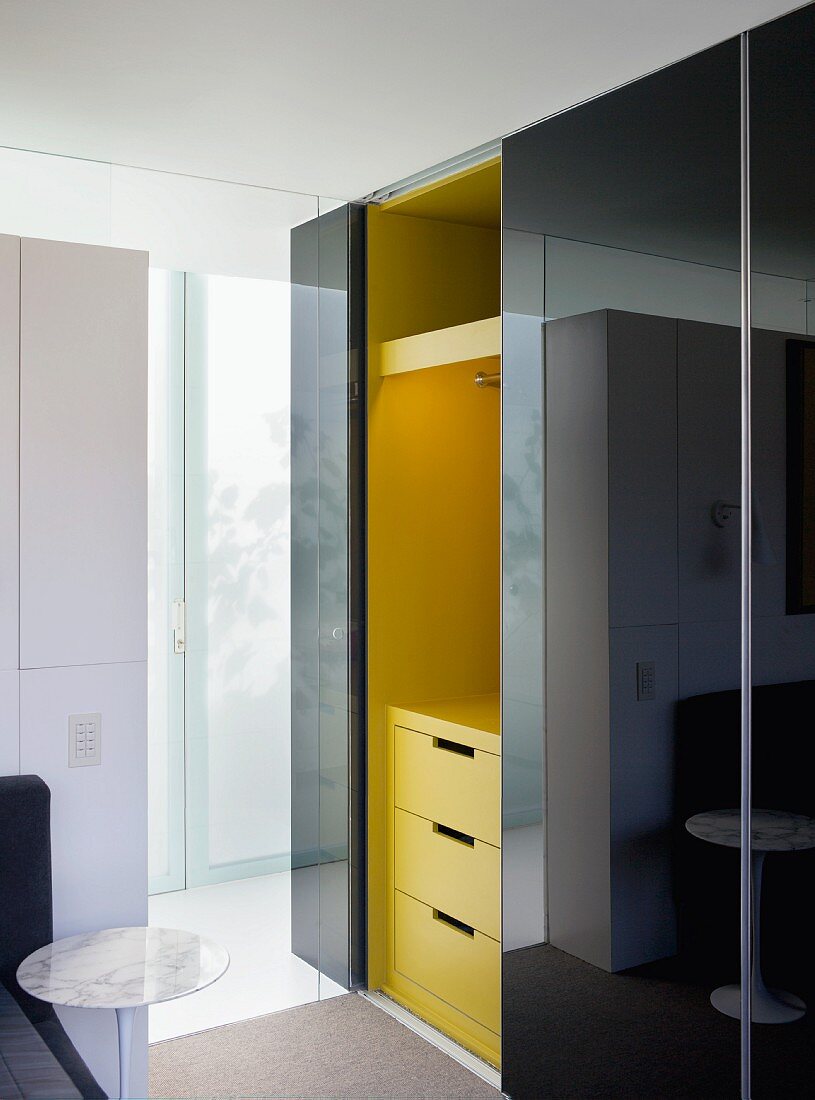 Dressing room with black, high gloss, sliding doors in front of a yellow cabinet unit