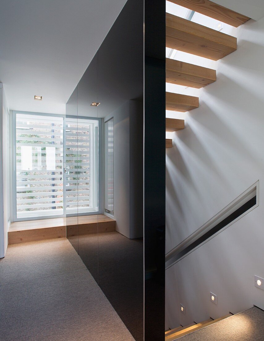 Schwarze hochglänzende Treppenhauswand und in Wand eingelassene Strahler neben Stufen