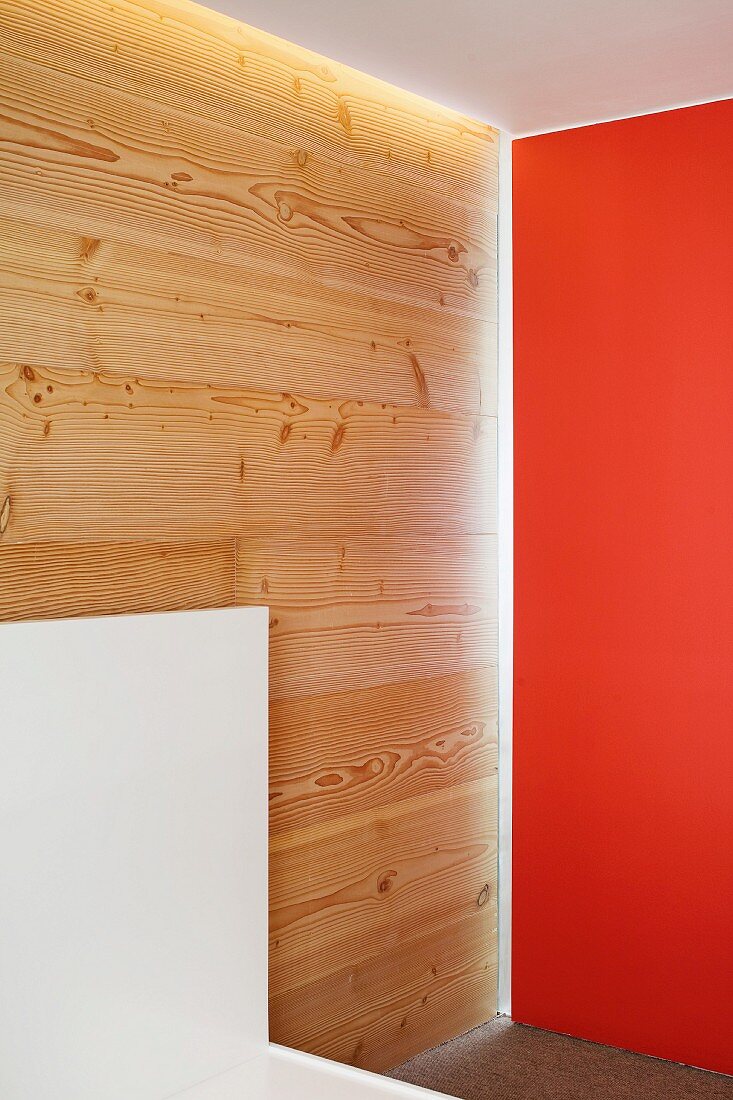 Corner of a room with one wall painted a shade of red and a wood paneled wall