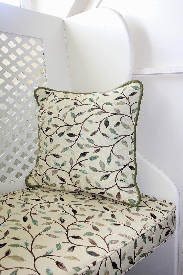 A decorative cushion on a white bench with a patterned seat