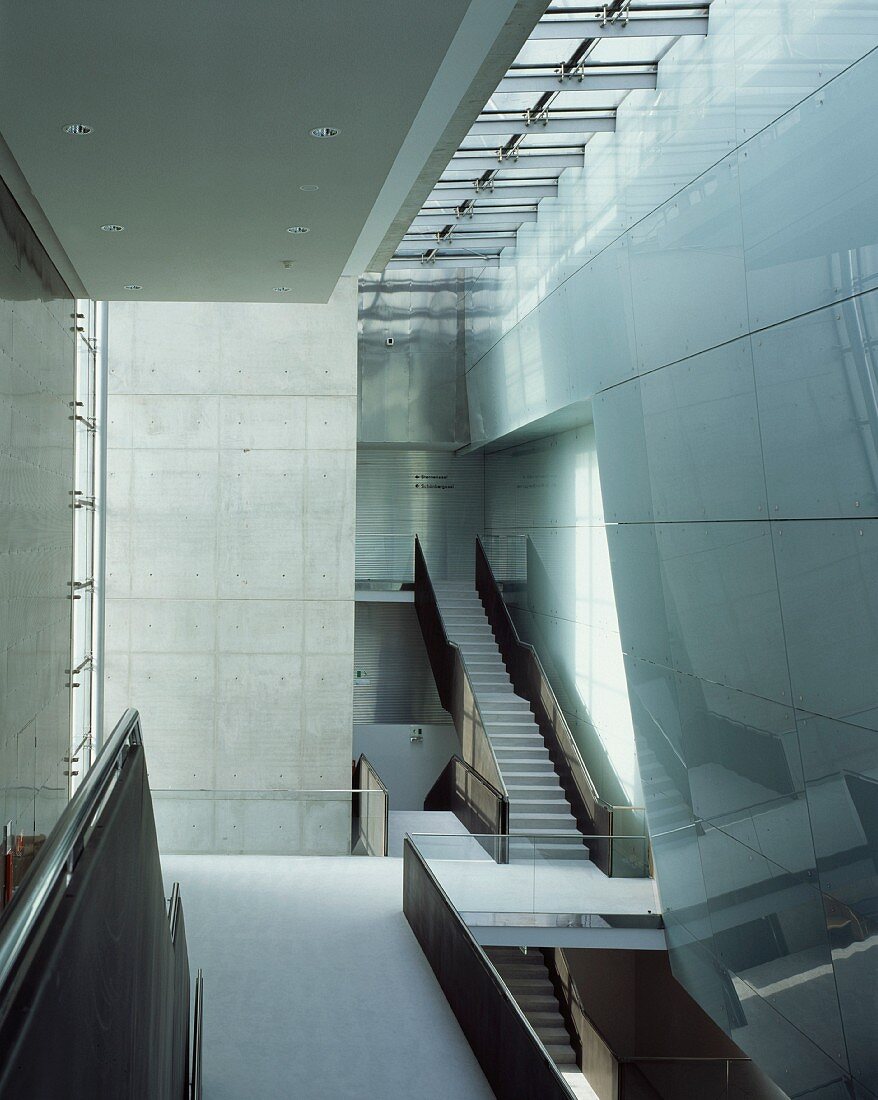 Flights of stairs illuminated through ceiling in tall, modern building with exposed concrete walls and reflective wall cladding