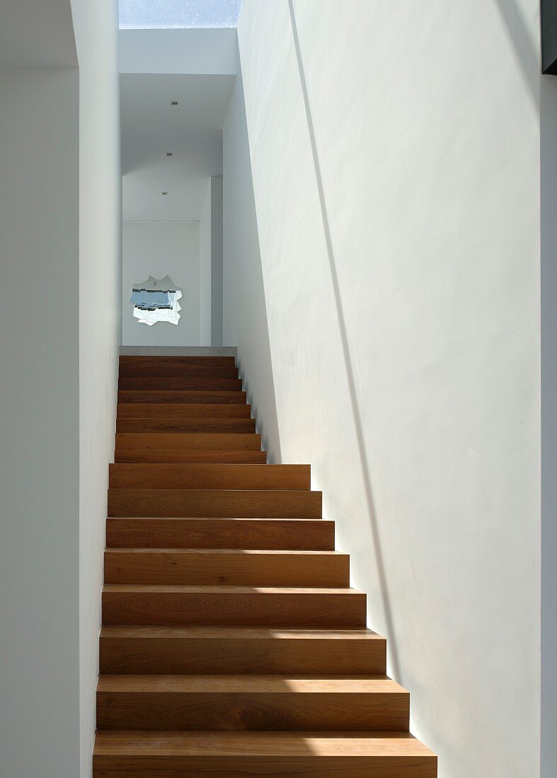 Schlichter Treppenaufgang aus hartem Tropenholz mit weissen Wänden und dekorativer, kleiner Wandöffnung
