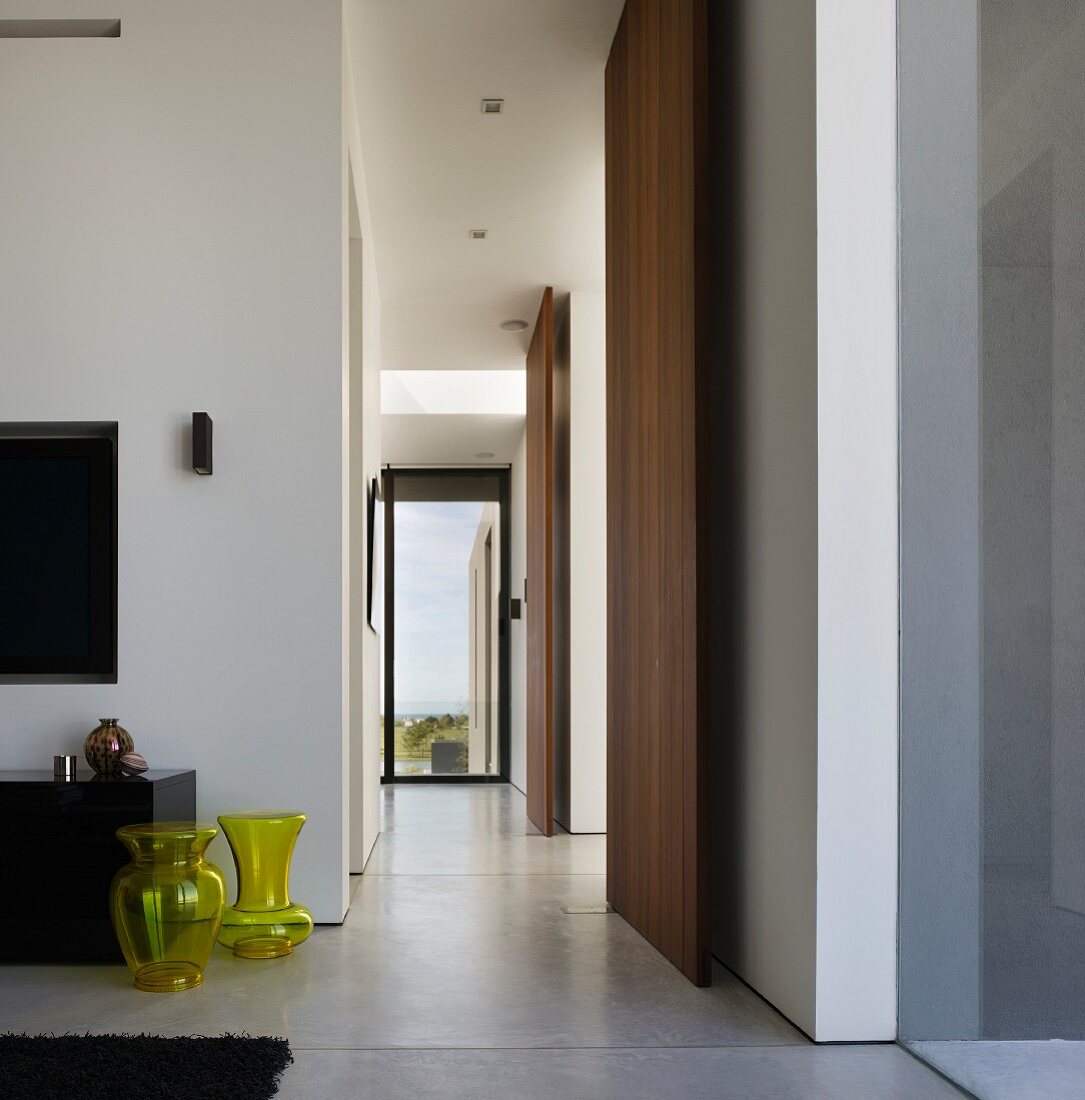Gangflucht in südamerikanischem Wohnhaus mit gelben Glasvasen auf poliertem Betonboden und raumhohen Paneelen aus exotischem Holz