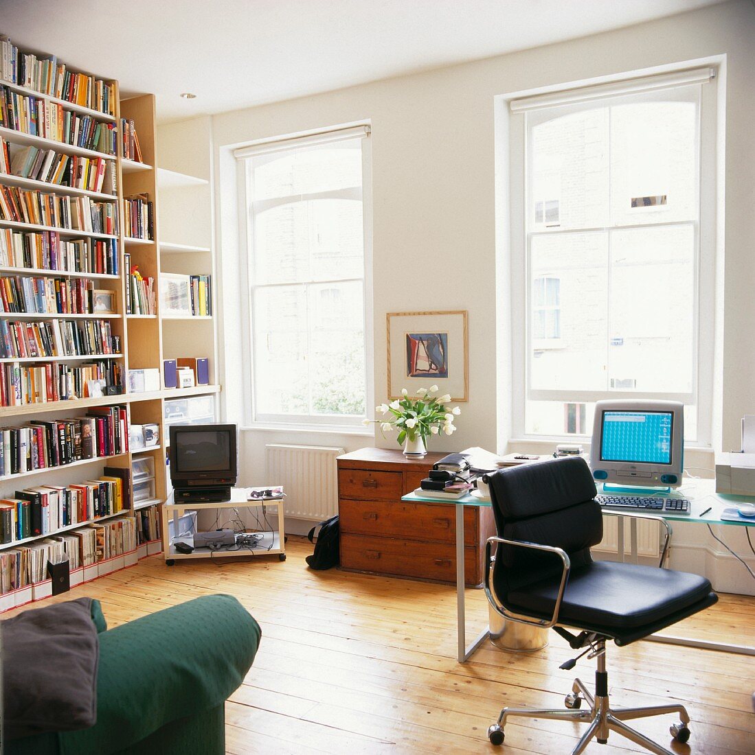 Bücherwand gegenüber home office mit schwarzem lederbezogenem Schreibtischstuhl vor Fenster im Wohnzimmer