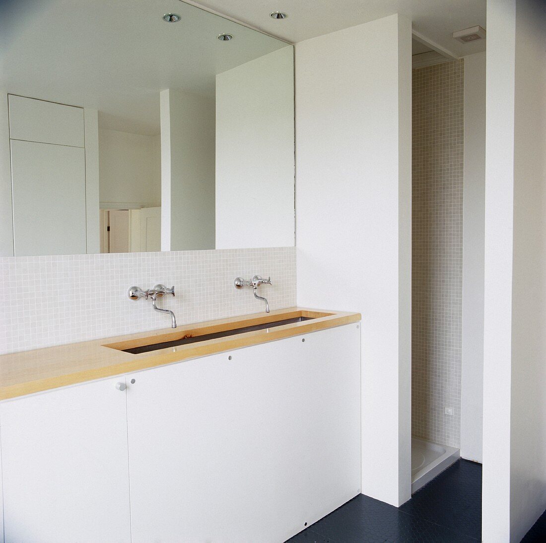 Schlichtes weisses Badezimmer mit heller Holzplatte auf Waschtisch vor vollflächigem Wandspiegel