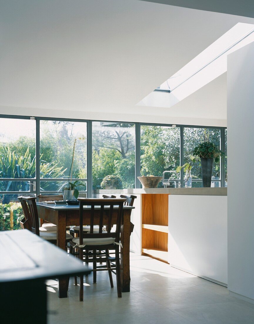 Esstisch mit Stühlen aus dunklem Holz in offener moderner Küche mit grosszügiger Fensterfront