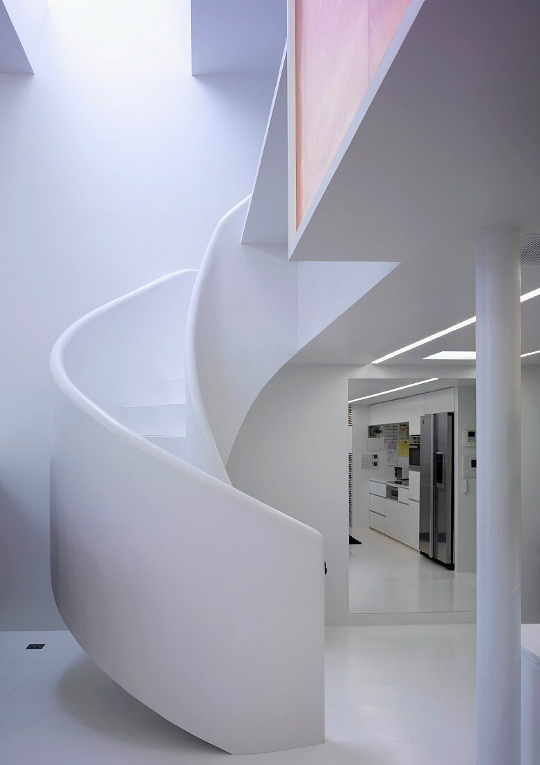 Curved staircase with white brick banister next to an open hallway with a view of the kitchen