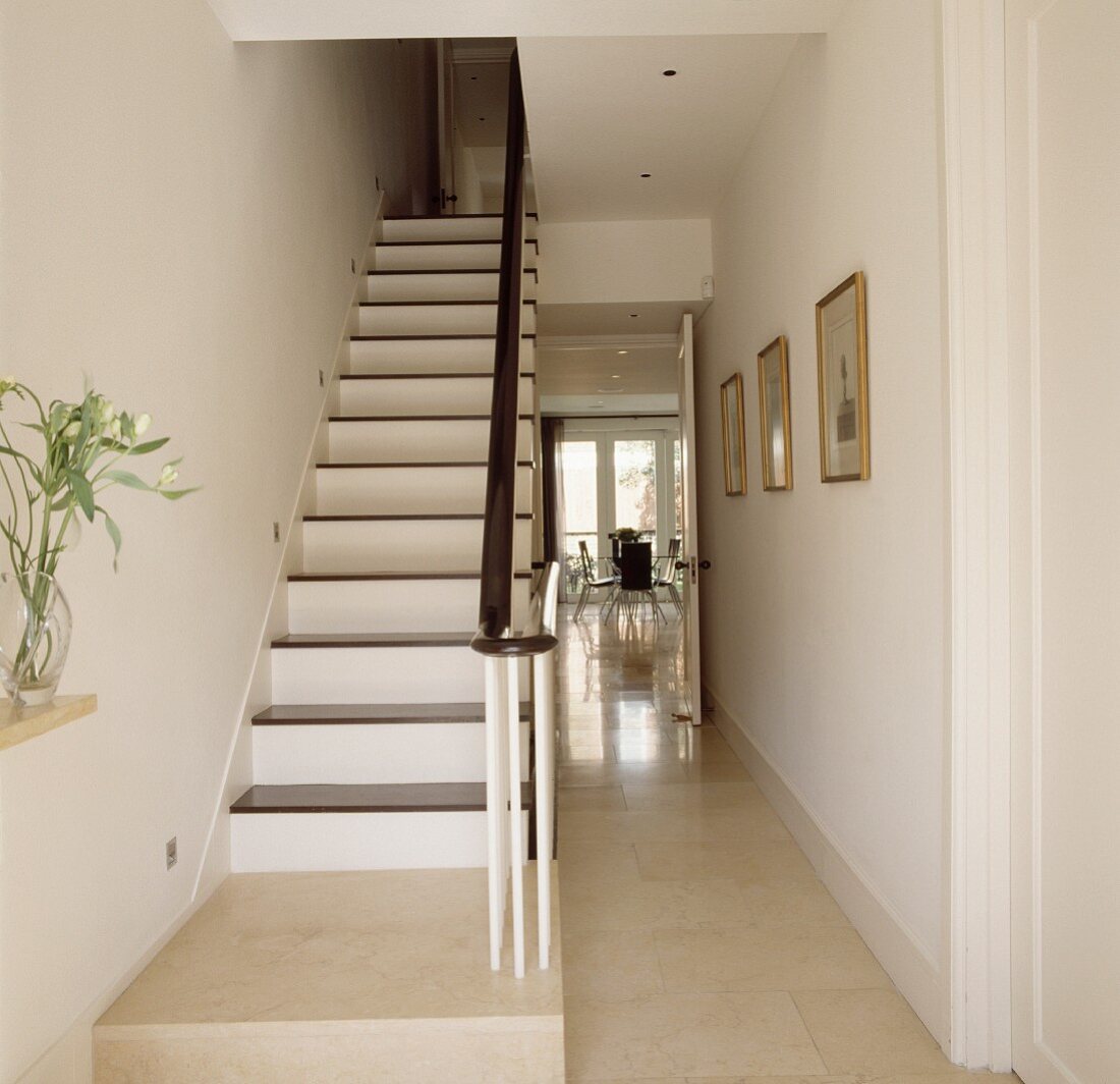 Schlichte weiss lackierte Holztreppe und dunkler Handlauf im Treppenhaus mit offener Tür und Blick in Esszimmer