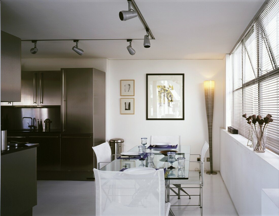 Set dining table and white sailcloth chairs in front of an open stainless steel kitchen