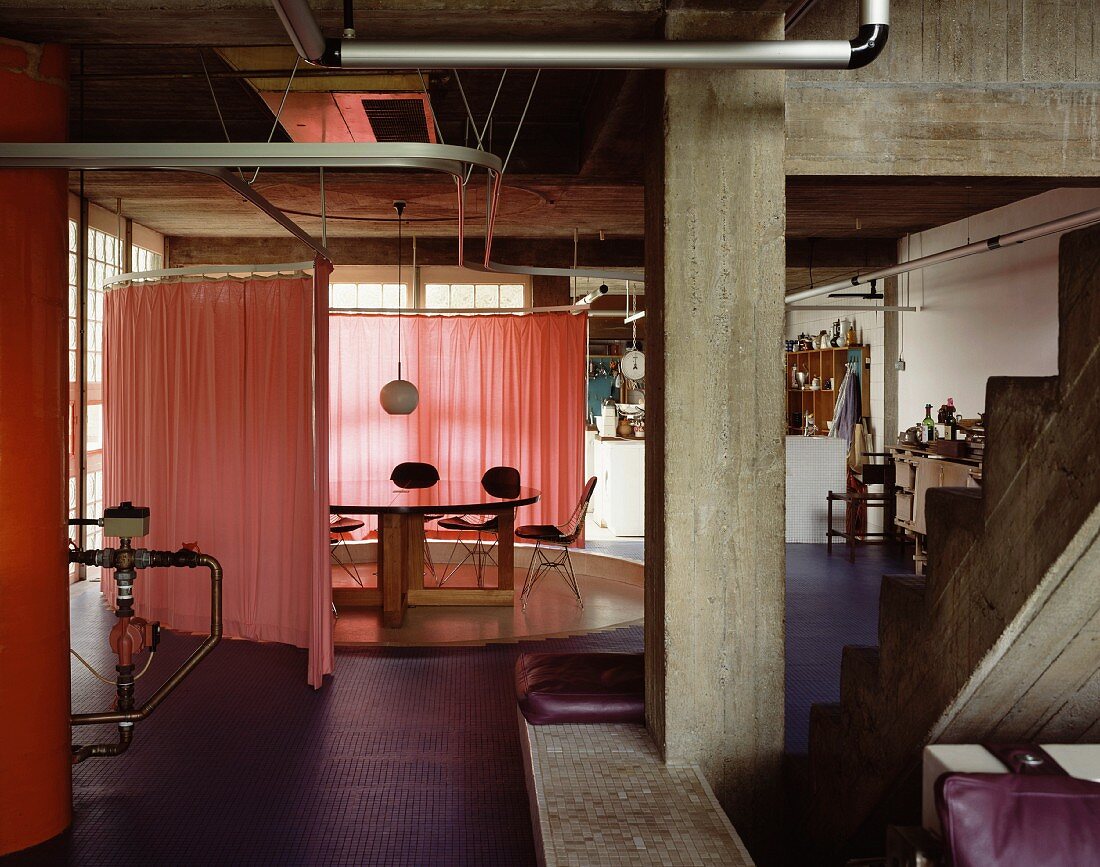 Industriehalle mit Betonkonstruktion und kreisförmiger Raumabtrennung um Esstisch mit rosa Vorhang