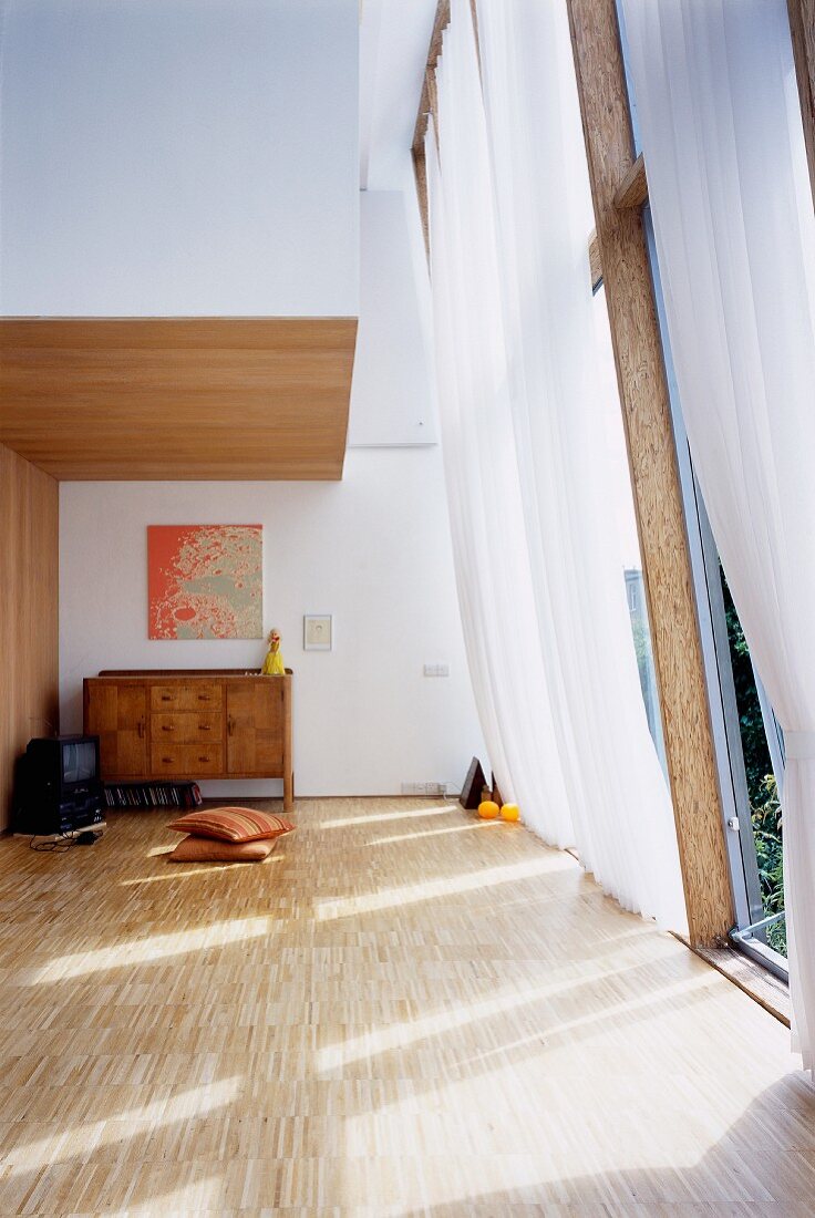 Minimalistischer Wohnraum mit luftigem Vorhang vor hohem Fenster