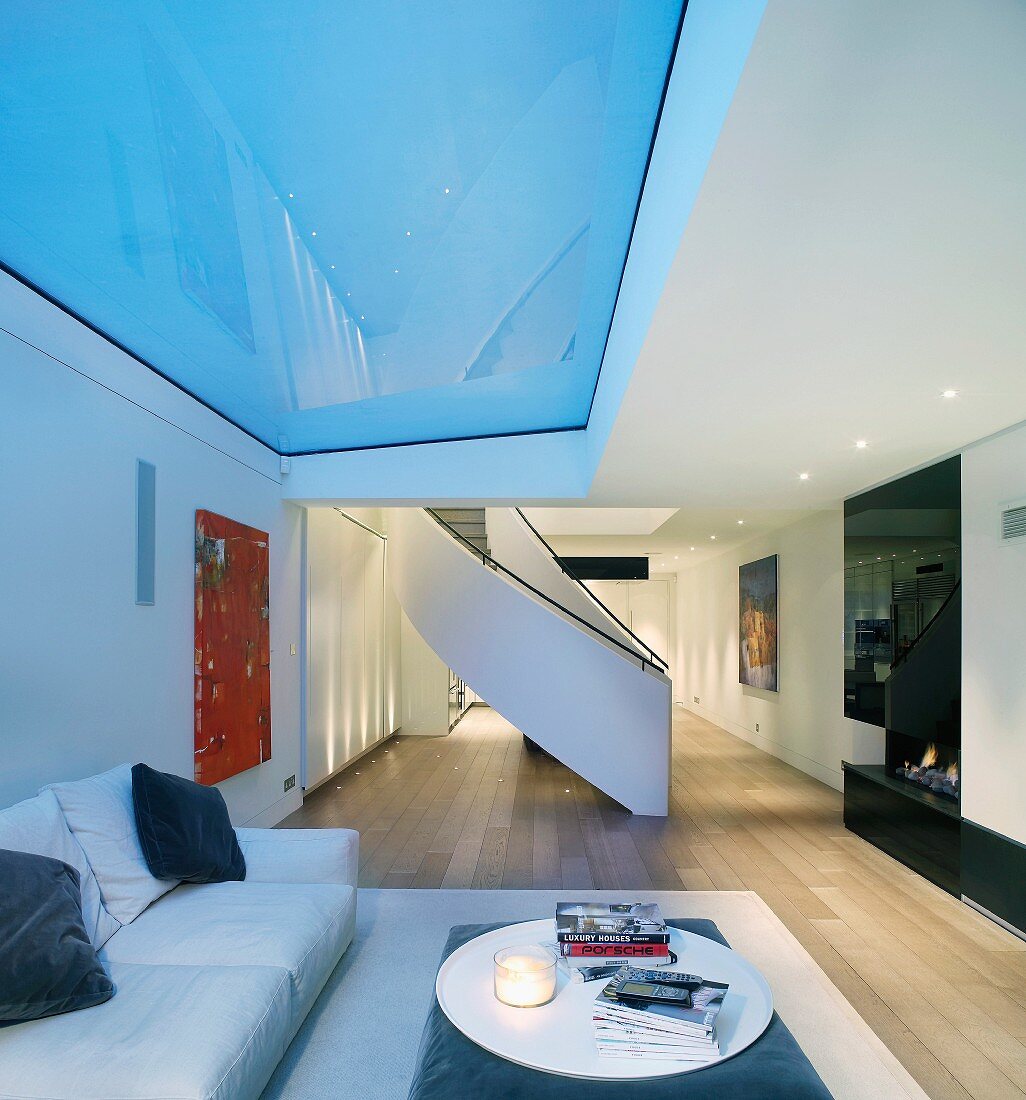 Moderner, offener Wohnraum mit geschwungener Treppe und Sofa unter Glasfeld in Decke
