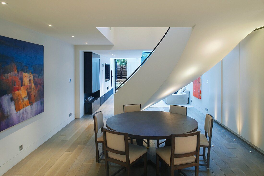 Essplatz mit rundem Tisch vor geschwungener Treppe im modernen Raum mit Bodenstrahlern im Dielenboden