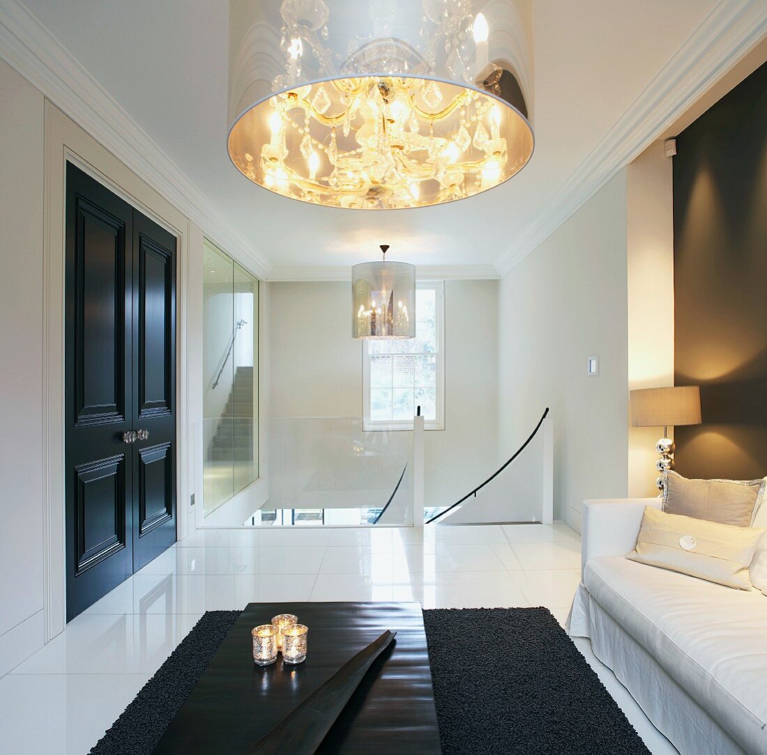 Modern living room with chandelier in transparent shade, black coffee table and open, white stairwell