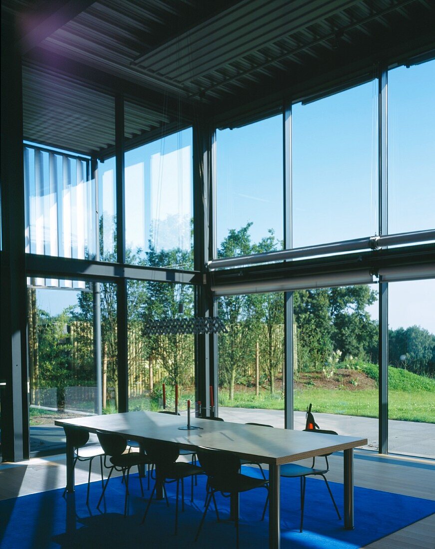 Esstisch mit Stühlen im Retrostil vor Glasfassade eines Neubauwohnhauses