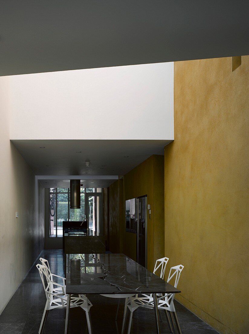 Kühles Ambiente - Esstisch und Stühle im Designerstil vor gelb getönter Wand im offenen Vorraum