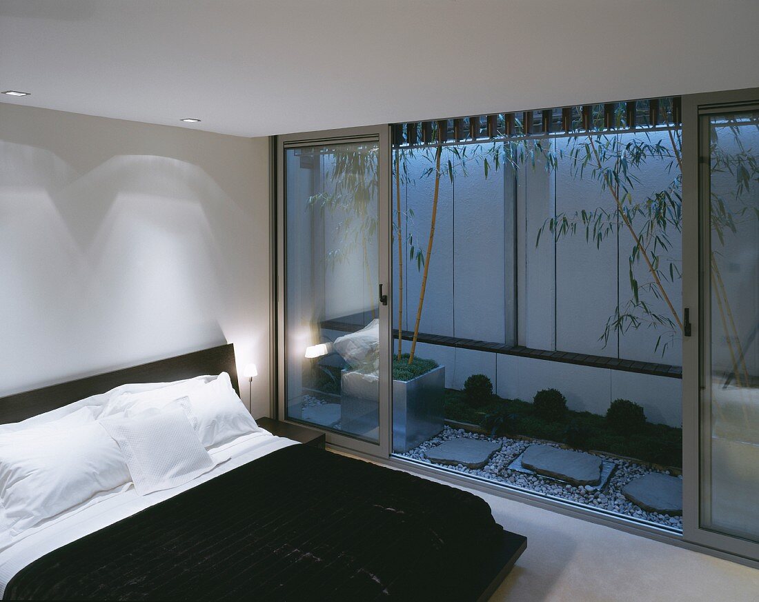 Modernes Schlafzimmer mit Doppelbett vor offener gestalter Terrasse in Abendstimmung