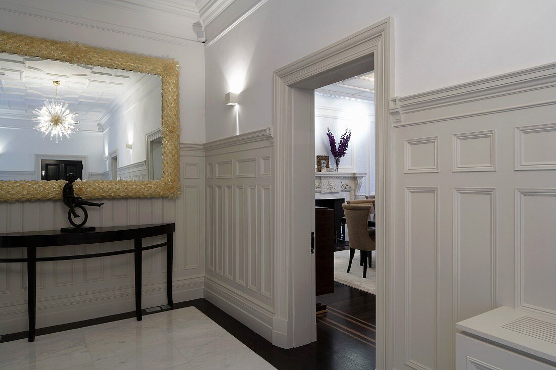 Lobby with white wood paneling on the wall and open living room door across from an antique console table with mirror