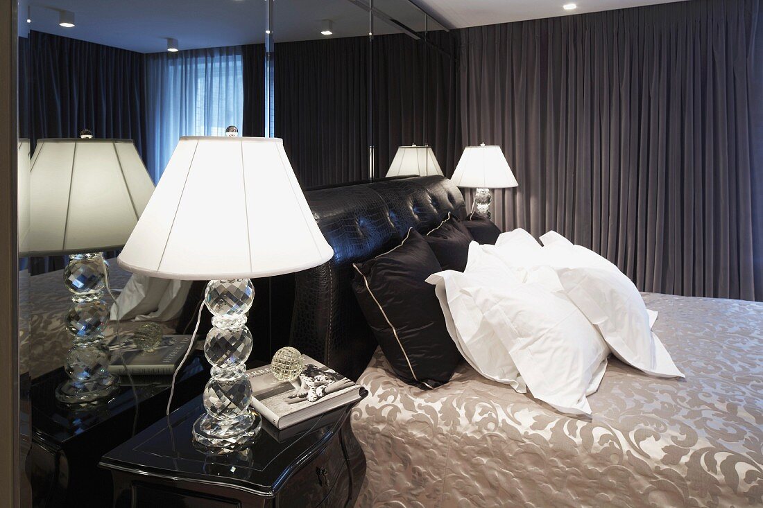 Herrenschlafzimmer mit Nachttischlampe neben weissen Kissen auf Doppelbett und dunkelgrauem Vorhang