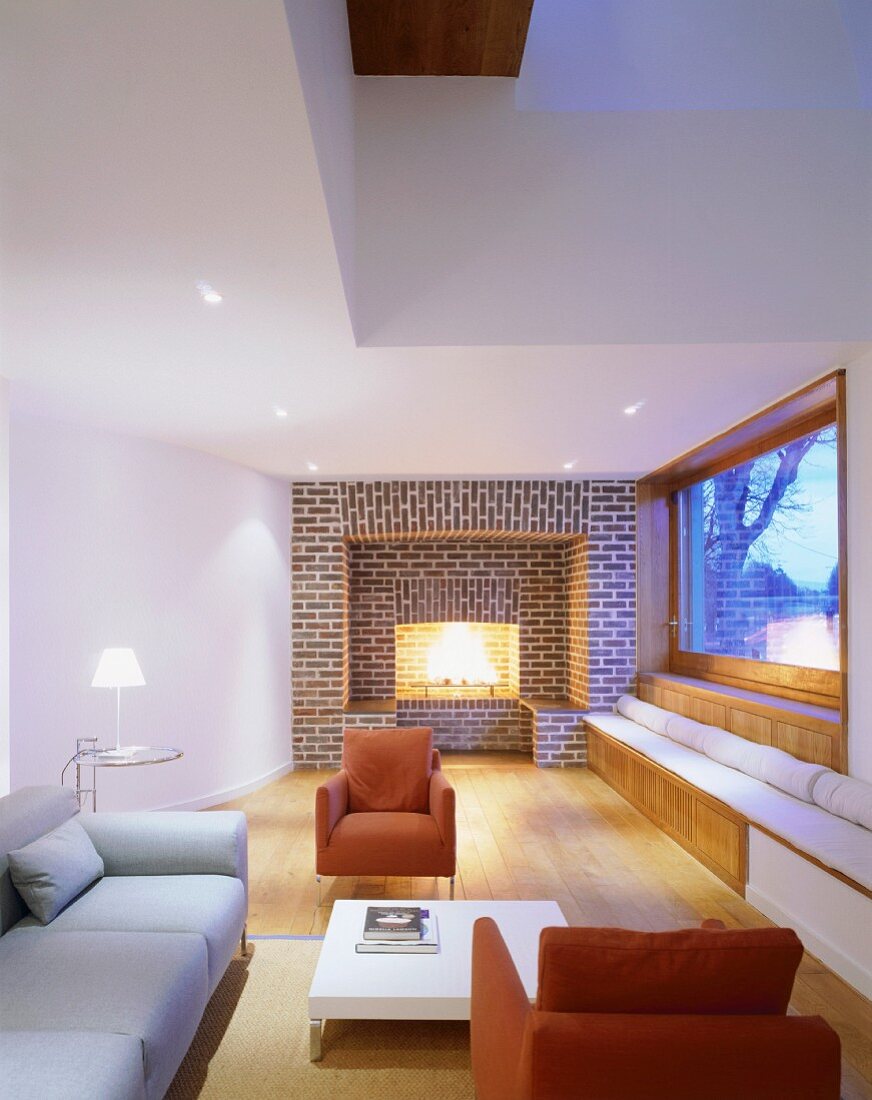 Schlichter Wohnraum mit farbigen Polstersesseln und Ziegelwand mit eingebautem Kamin
