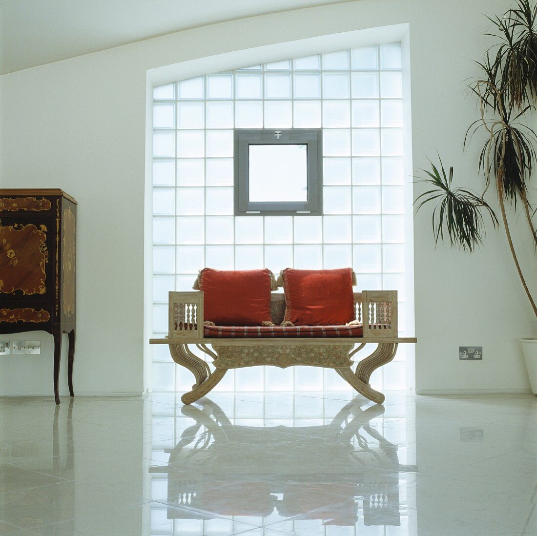 Antique, English bench with red cushion in front of a glass brick wall and reflective tile floor