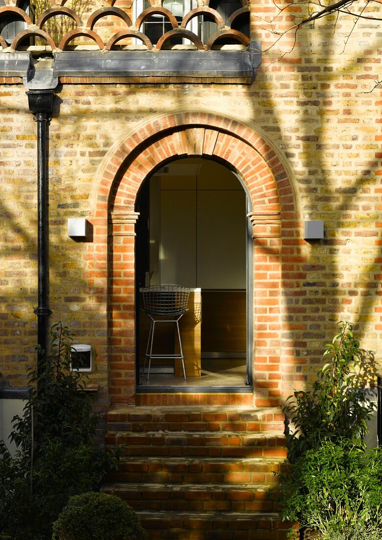 House facade with brick round arch and view through an open door into the kitchen