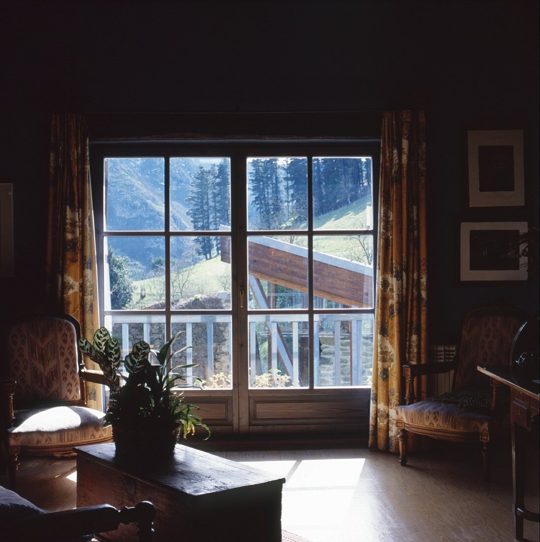 Dark living room with baroque armchairs beside balcony doors and a view of the mountains