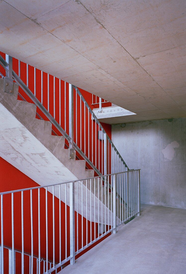 Treppenhaus aus Beton mit rot getönter Wand und Metallgeländer an Betontreppe