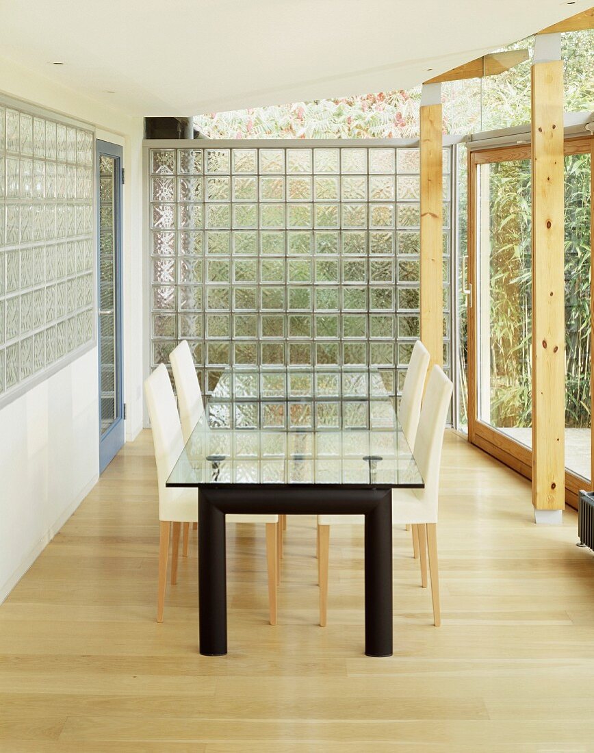 Glass top dining table and upholstered chairs in front of a glass brick wall