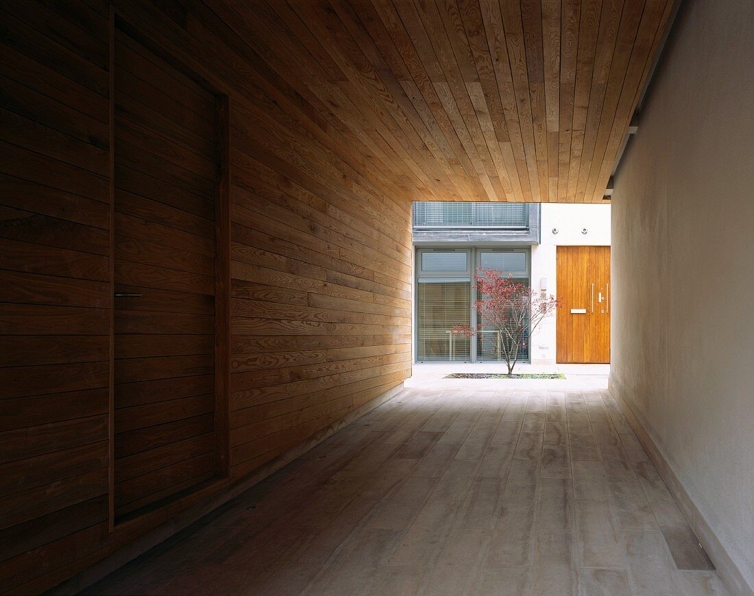 Holzverkleideter Durchgang und Blick auf Baum im gestalteten Innenhof