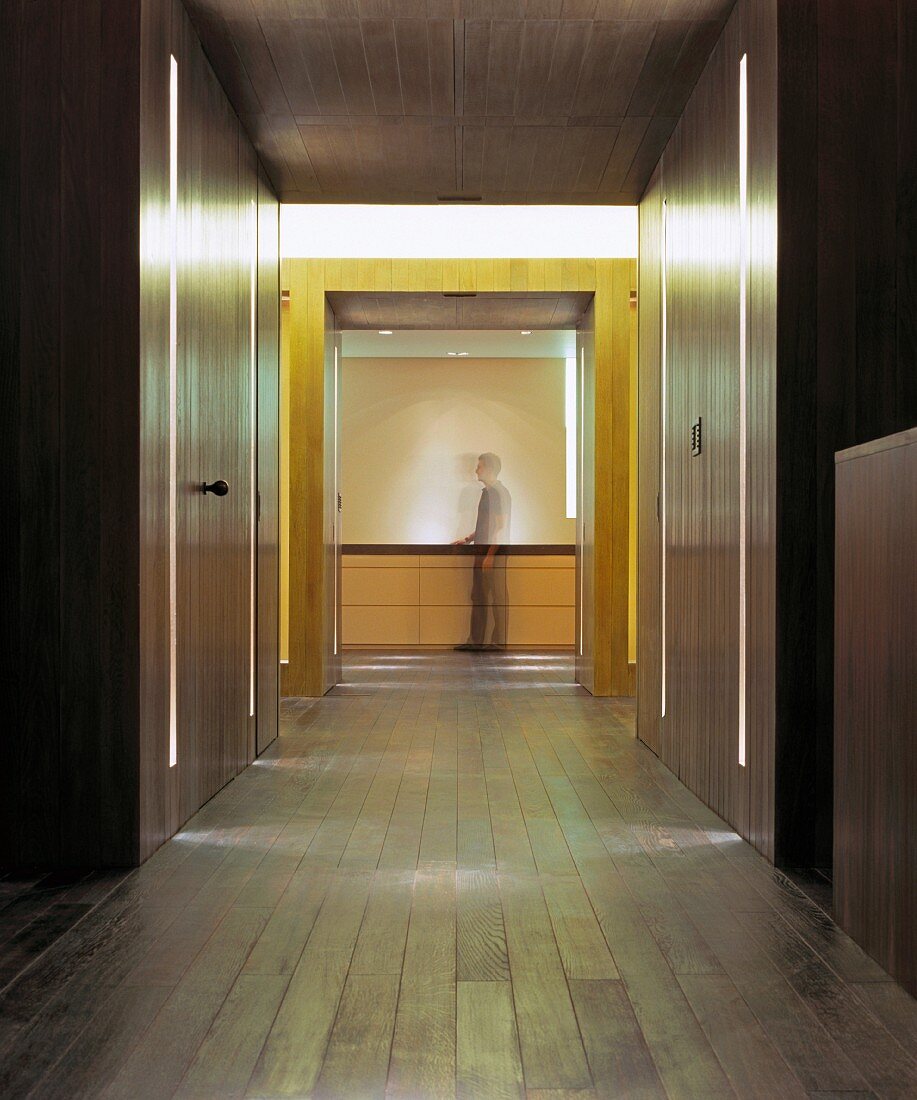 Moderner minimalistischer Vorraum mit Einbauschränken aus Holz und integrierten Lichtbändern und Blick auf Mann vor Sideboard