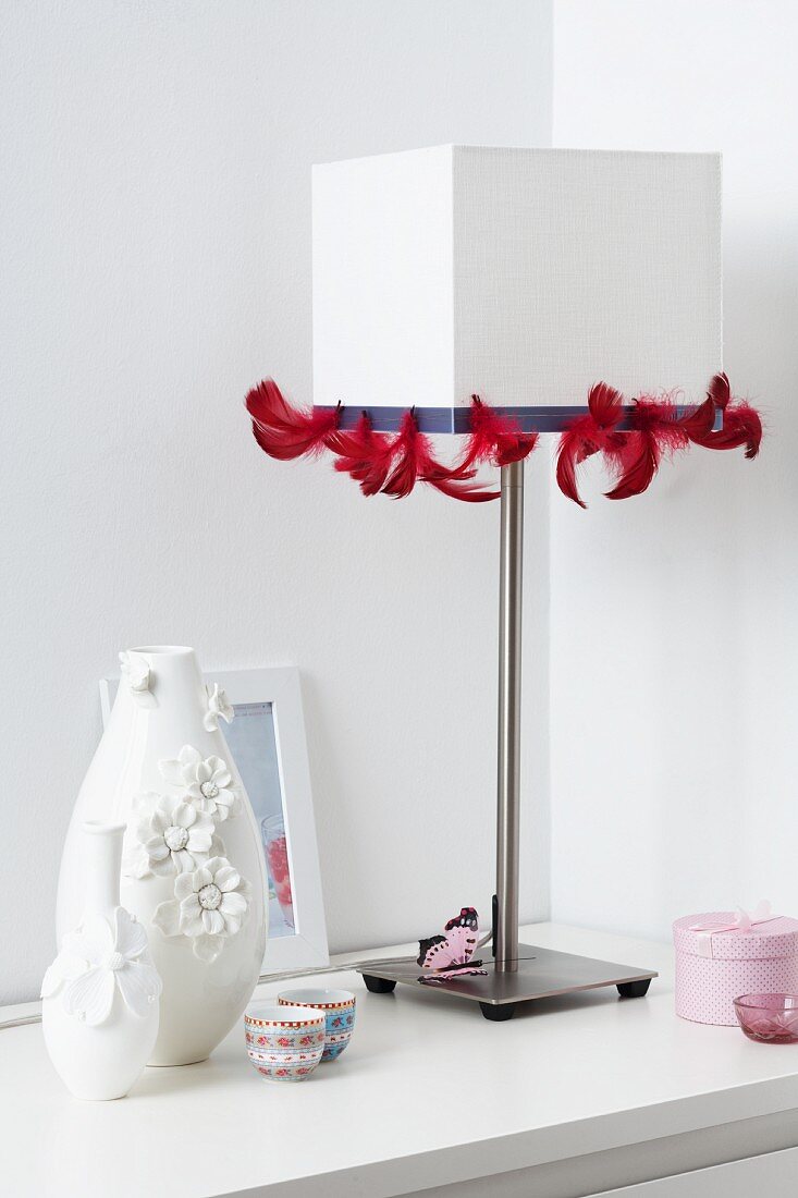 A white table lamp decorated with red feather ribbon and vases decorated with flowers