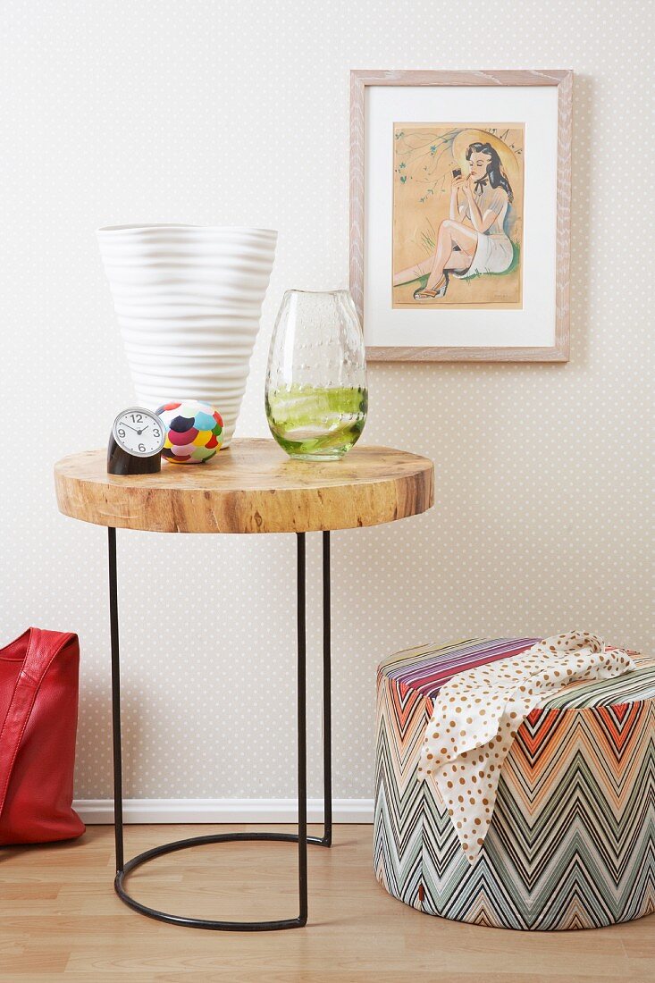 Vasen und Wecker auf einem runden Tisch mit Holztischplatte, ein Hocker und ein Bild an der Wand