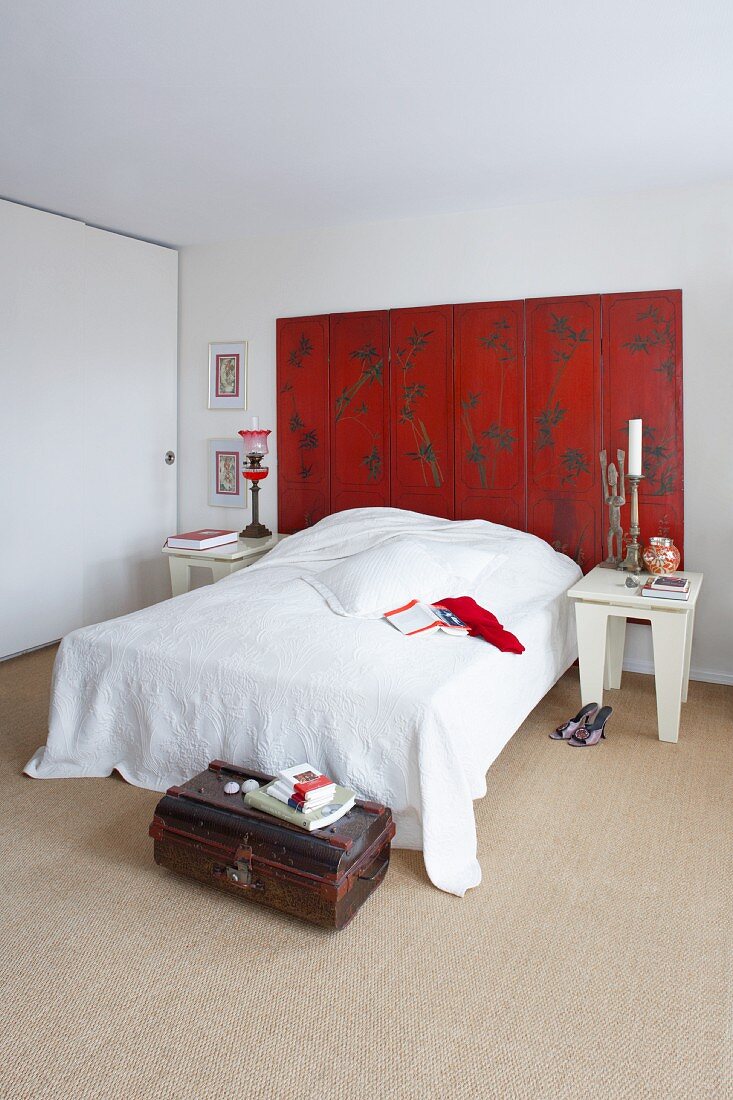 Weisses Schlafzimmer mit rotem Paravent am Bettkopf