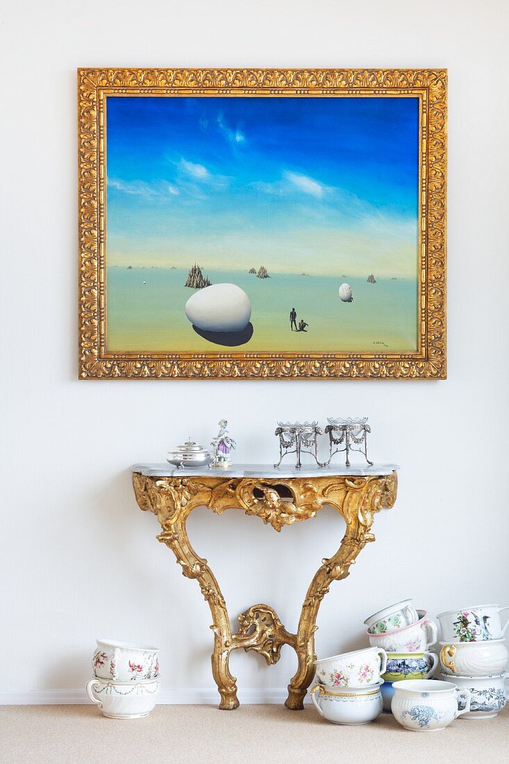 Goldgerahmtes Bild über einem Wandtisch im Rokoko-Stil und Porzellangeschirr