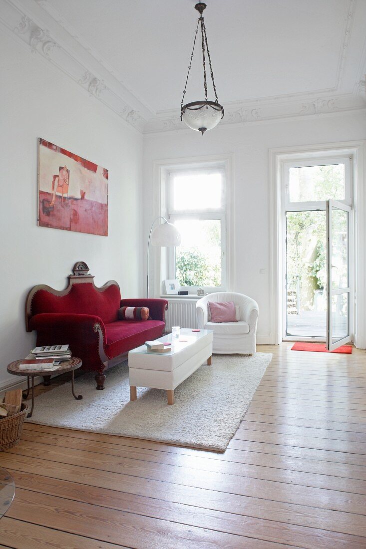 Blick in ein Wohnzimmer mit dunkelrotem Samtsofa, weißem Sessel und Couchtisch