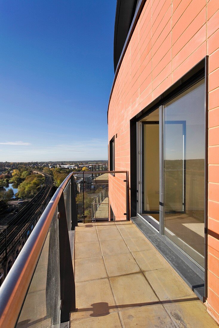 Balkon mit Steinfliesen vor modernem Haus mit Fensterfront und Blick in die Umgebung