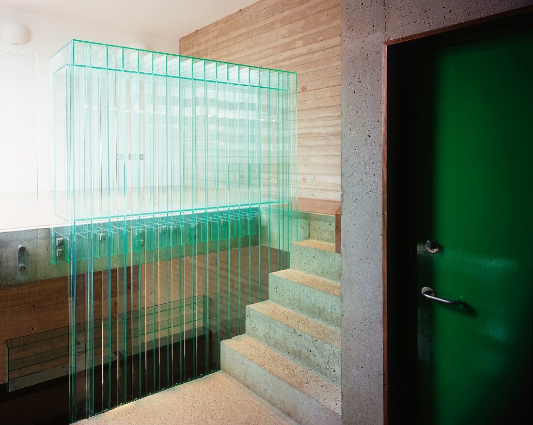 Grün lackierte Wohnungstür im Treppenhaus aus Beton und Brüstungswand aus Glaslamellen