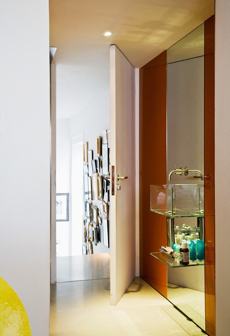 Designer Waschbecken aus Glas mit Ablage vor raumhohem Spiegel und offener Badtür