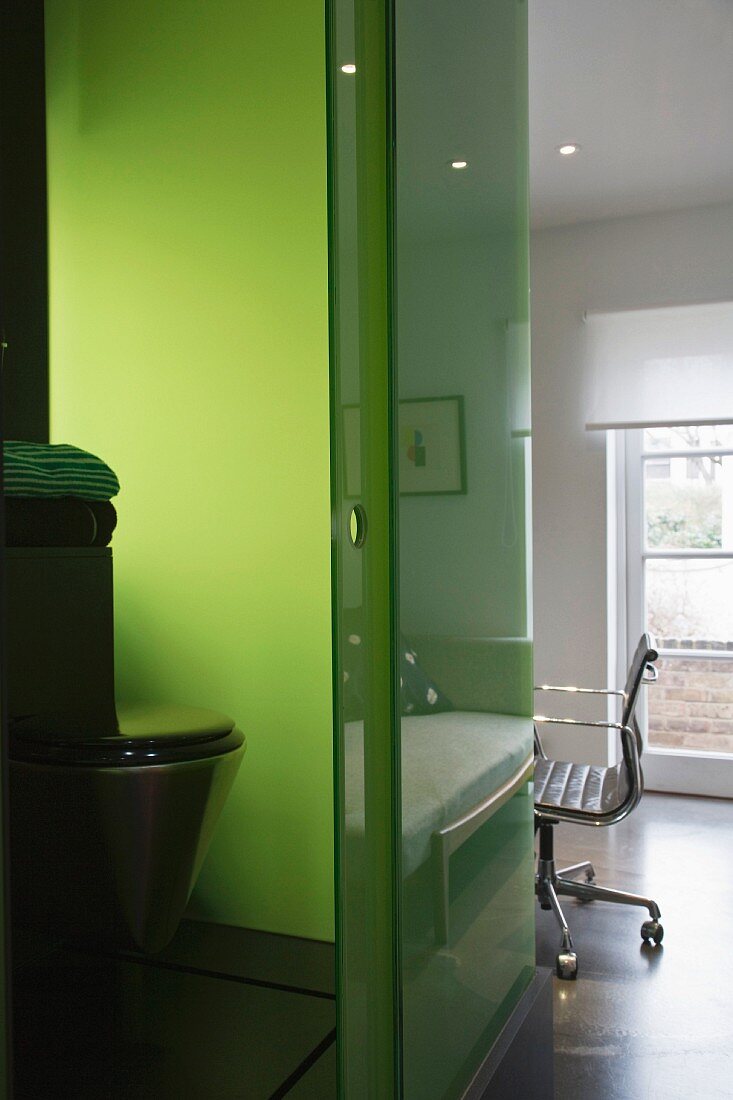Blick ins offene Bad auf Toilette vor grün gefärbter Glaswand