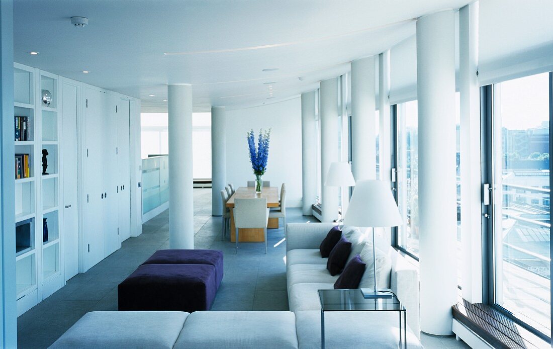A modern penthouse with an open-plan living room and dining room and white concrete pillars