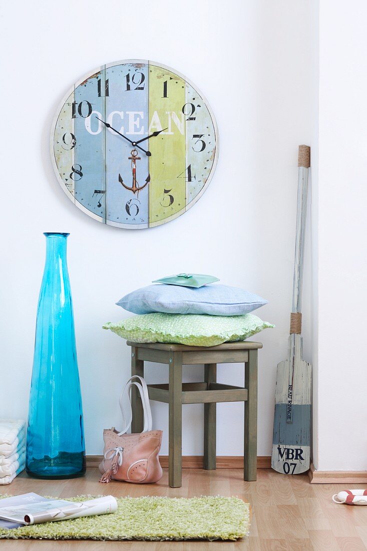 Grosse Wanduhr, blaue Bodenvase, Stuhl mit Kissen und ein Paddel