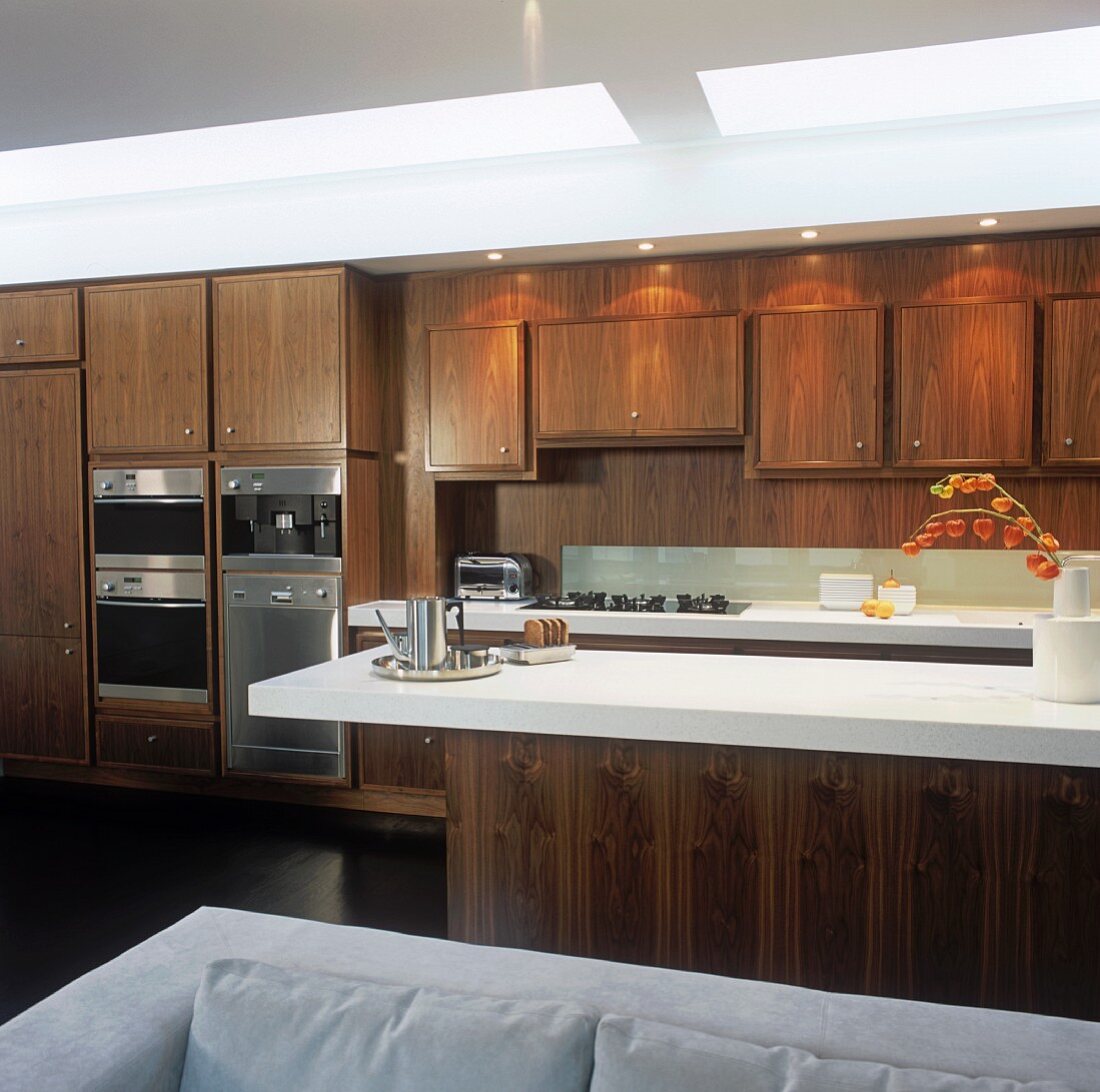 An open-plan fitted kitchen with wooden cupboards and a bar with a white surface