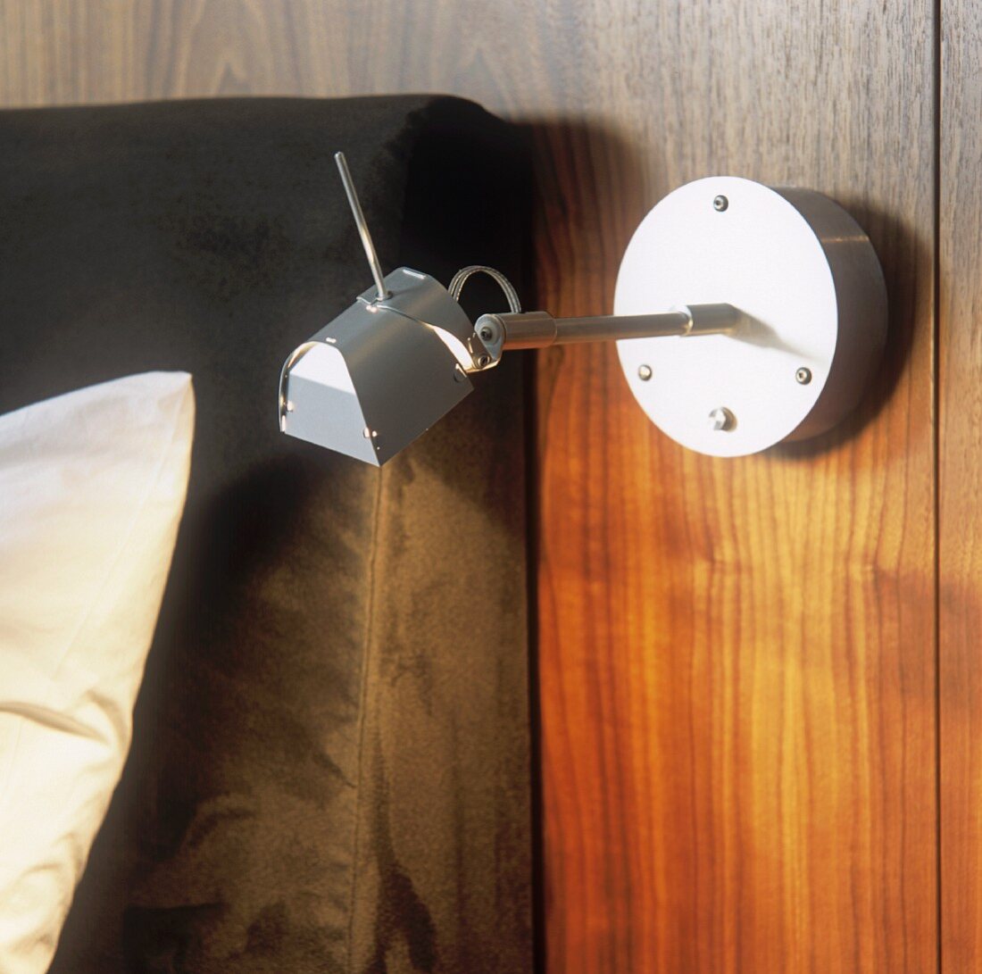 A modern, swivel bedside lamp made of stainless steel and mounted on a wooden panel