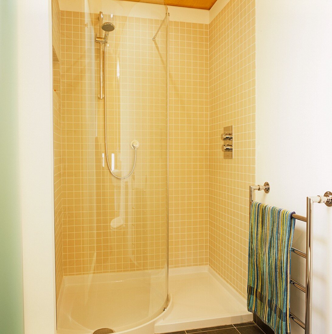 Gelbgeflieste Dusche mit gebogener Glastrennwand und Handtuchtrockner aus Edelstahl