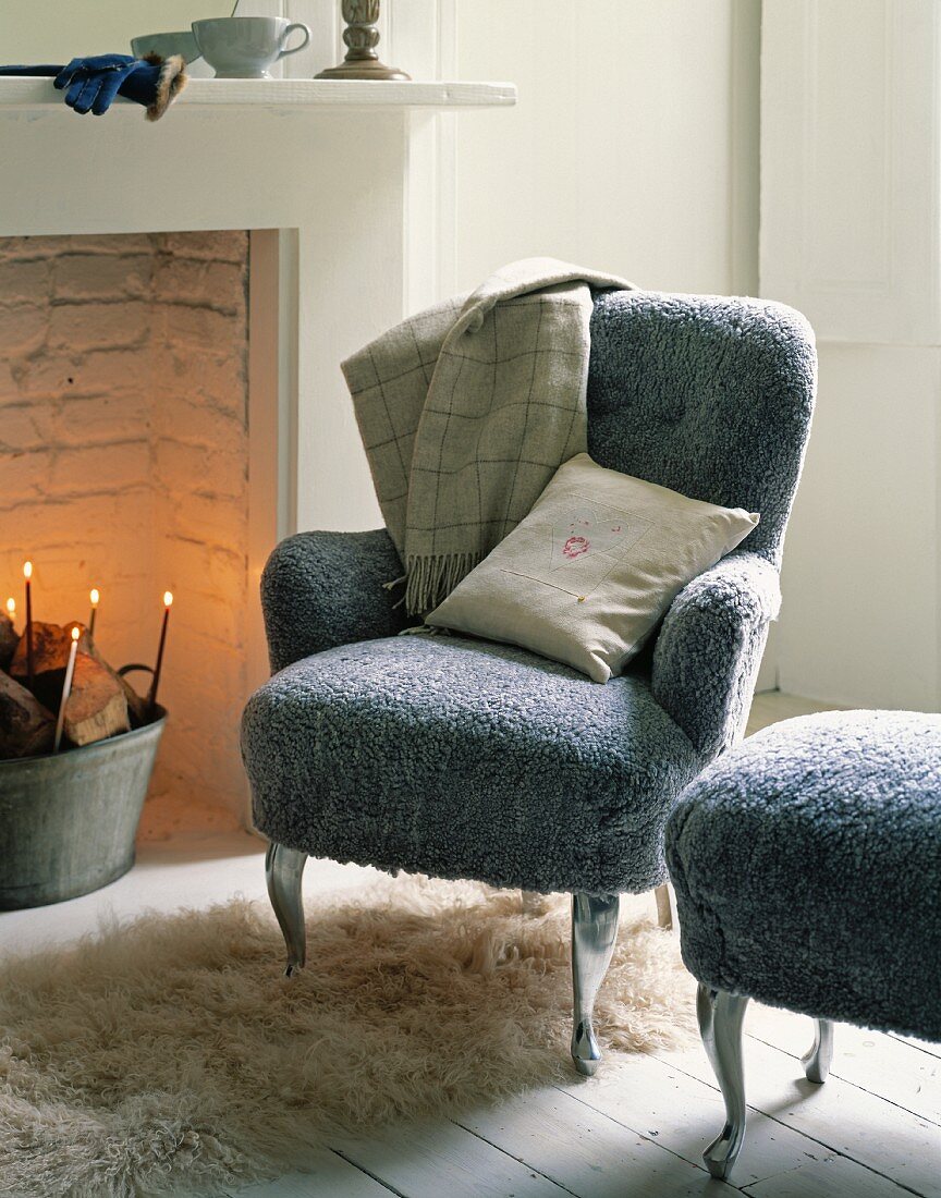 Sessel und passender Hocker mit grauem flauschigen Bezug neben Kamin im traditionellem Ambiente
