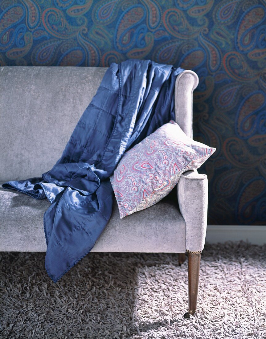 Blaue Satintagesdecke auf fliederfarbenem Sofa und Flauschteppich