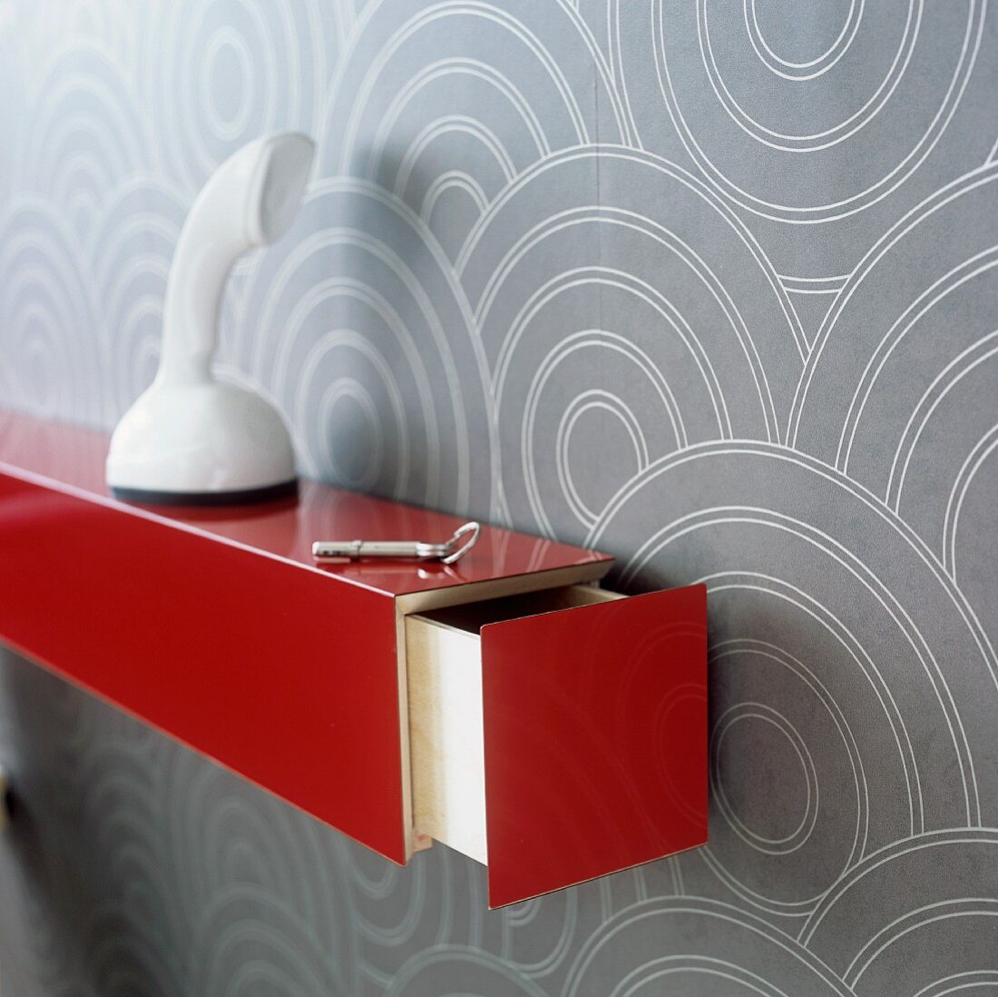 Rot lackierte Konsole mit geöffneter Schublade und weisses Telefon vor Tapete mit geometrischen Muster an Wand